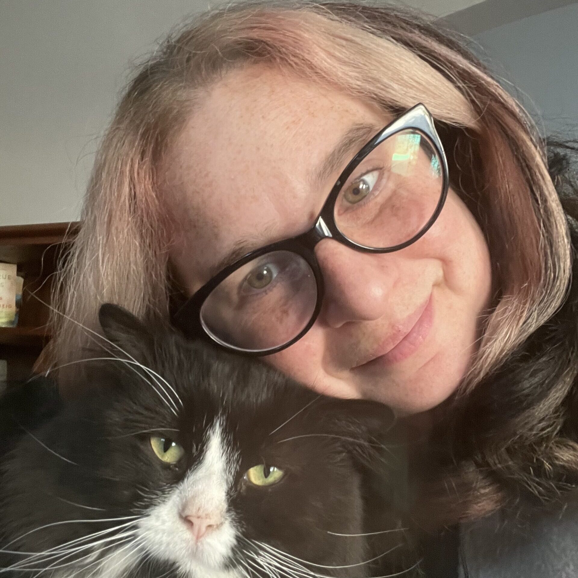 A white woman with black cat-eye glasses and a cute tuxedo cat